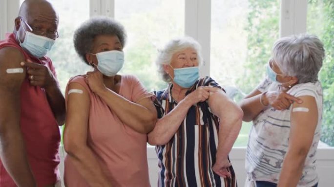 一群戴着口罩的多元化老年人在家里展示了接种疫苗的肩膀