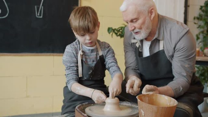 专业的波特高年级男子在工作室教男孩在投掷轮上制作陶瓷花瓶