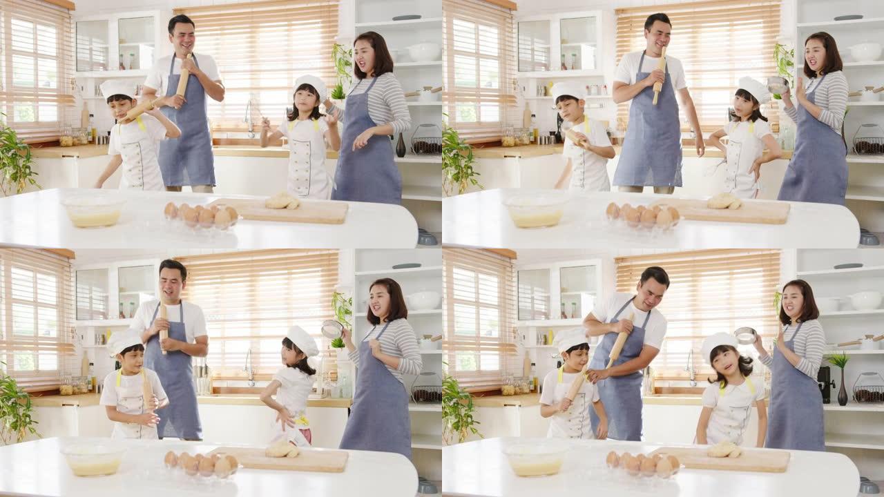 快乐的年轻亚洲家庭和学龄前的孩子有乐趣听音乐和跳舞，同时在早上在厨房家里做早餐的烘焙糕点。