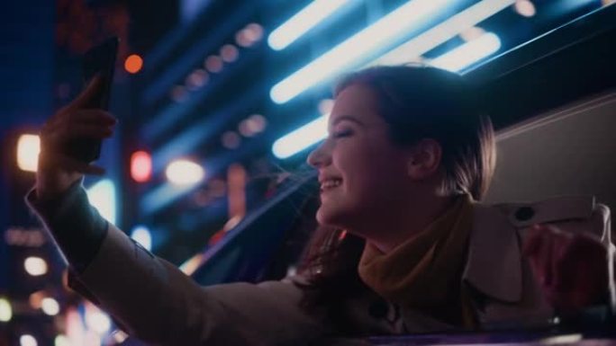 晚上，兴奋的女性从汽车后座望向窗外。女人在智能手机上拍照和录像，惊讶地发现带有工作霓虹灯的城市街道多
