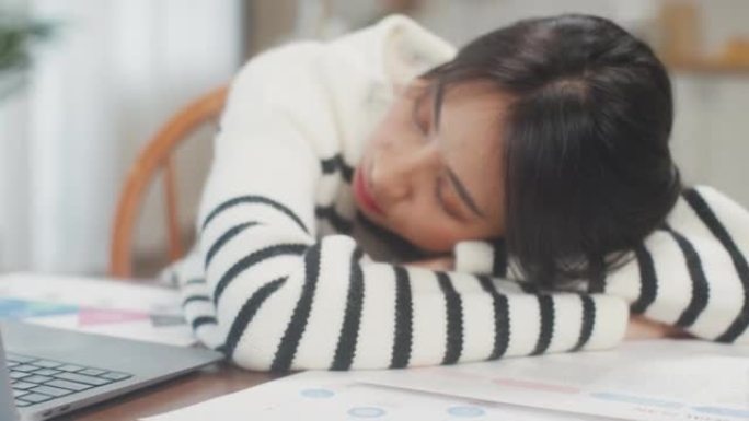 自由职业者亚洲精疲力尽的女士努力工作，在家中用木桌上的许多纸睡觉。在家从客厅工作，远程，社交距离，检