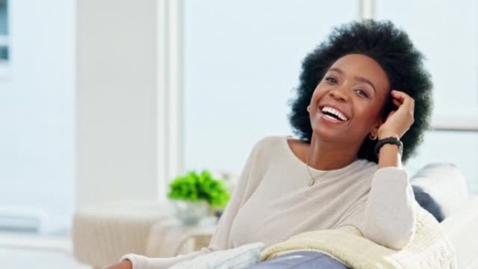 一个快乐的非洲女人周末在家沙发上放松的肖像。美丽休闲的非洲裔美国女孩微笑着，在她明亮的客厅享受一个轻