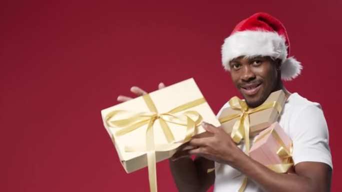 一个戴着圣诞帽的黑皮肤快乐的男人拿着一堆礼品盒微笑着