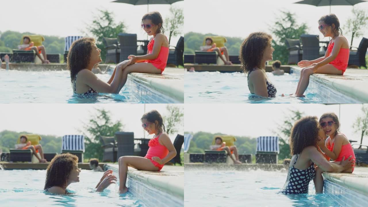 暑假期间，母亲在室外游泳池里玩得开心，女儿戴着心形太阳镜坐在边缘 -- 慢动作拍摄