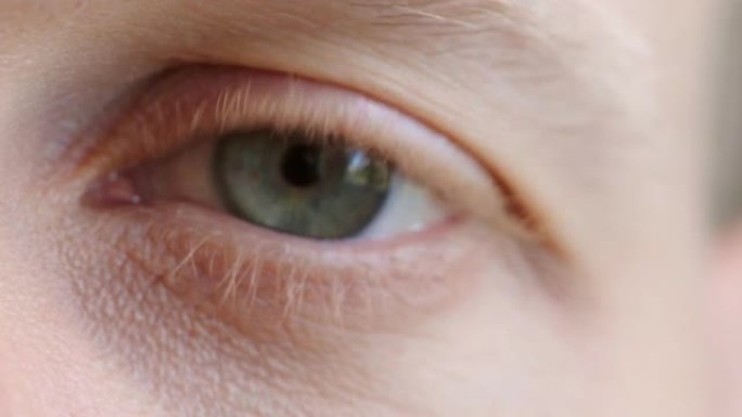 视力测试过程中绿色眼睛闪烁的特写镜头。验光过程中人类眼球观察虹膜或视力的解剖细节。年轻金发男子，皮肤