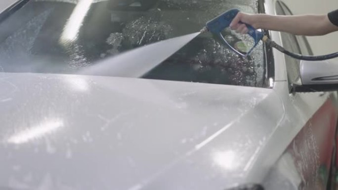 汽车清洁剂用高压水喷射清洗白色汽车。