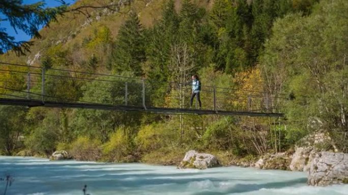 年轻女子越过绿松石山河上的木制吊桥