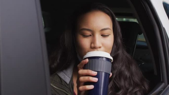 戴着低面罩的亚洲女人看着窗外，坐在车里喝咖啡