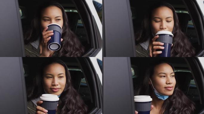 戴着低面罩的亚洲女人看着窗外，坐在车里喝咖啡