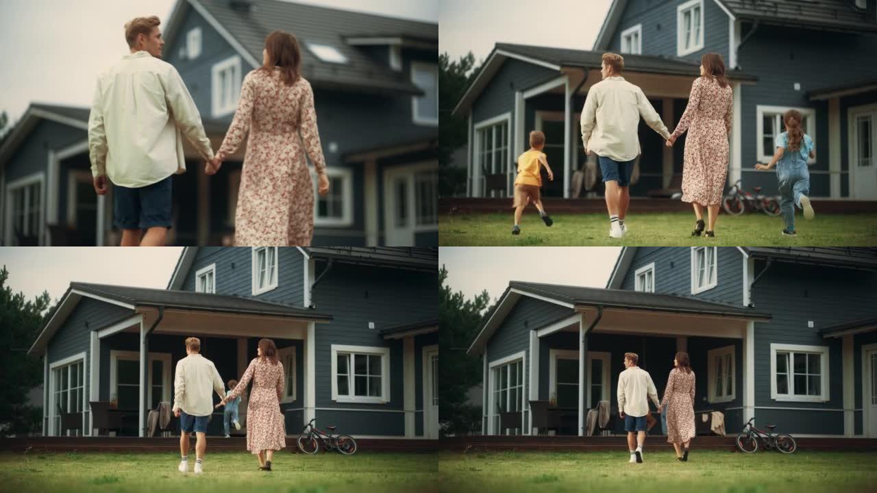 年轻美丽的夫妇牵着手在户外走向乡间别墅。他们的小儿子和女儿和他们一起跑步。年轻的现代家庭在家，后面的