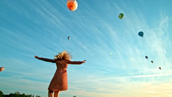 超级慢动作女人在飞舞的热气球前在地面上旋转