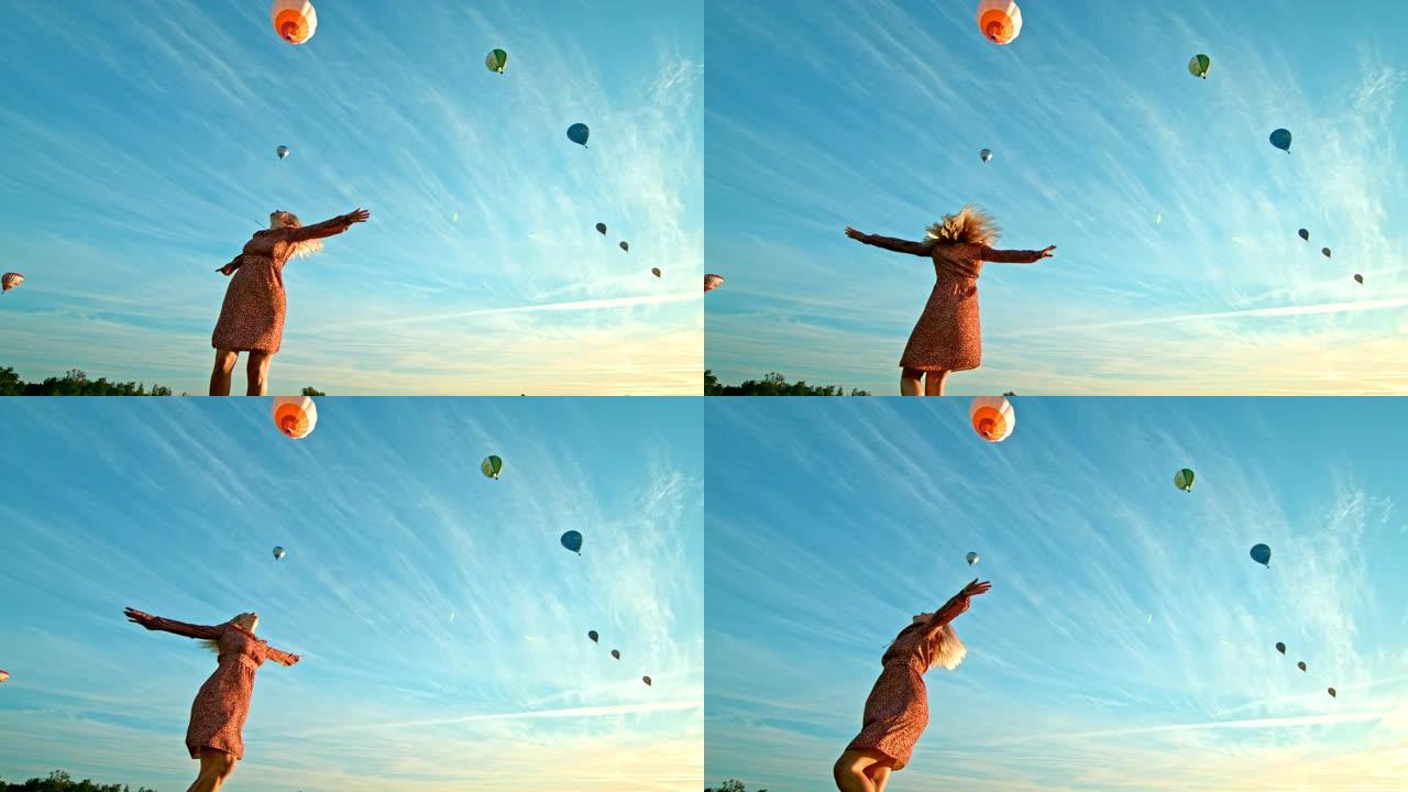 超级慢动作女人在飞舞的热气球前在地面上旋转