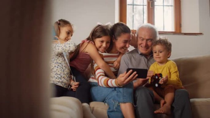 快乐的小家庭坐在客厅的沙发上，在智能手机上进行视频通话。三代人通过互联网与远亲建立联系，与技术保持联