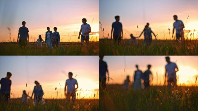 SLO MO家庭带着三个孩子在日落时在草地上行走