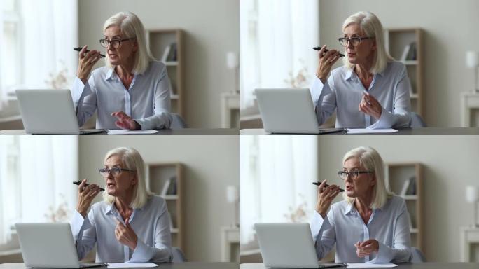成熟的女商人坐在工作场所的免提电话上讲话
