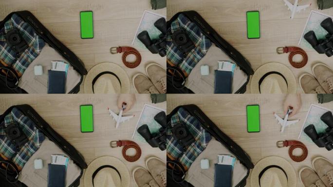 带有绿屏色度键智能手机的行李箱和门票旁边的男性手着陆玩具飞机的特写