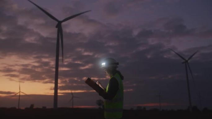 穿着制服的工程师在黄昏时在风力涡轮机农场工作