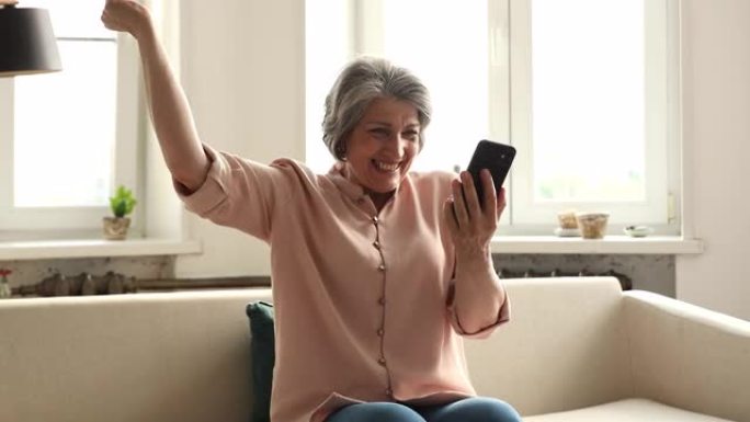 年长的女人在手机上阅读短信庆祝成功感到喜出望外