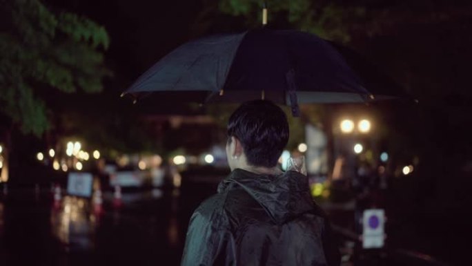 年轻人在下雨的时候穿雨衣。在伞下。外面很黑，正在下雨