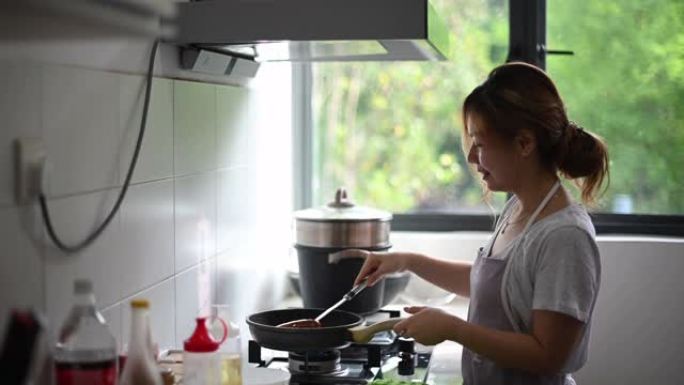 一位亚洲中国美女在厨房里煎鸡蛋准备吃早餐