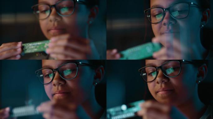 一个可爱的年轻的多种族黑人女孩的特写肖像正在研究一个小型印刷电路板对象。年轻的女性戴着眼镜，从事她的