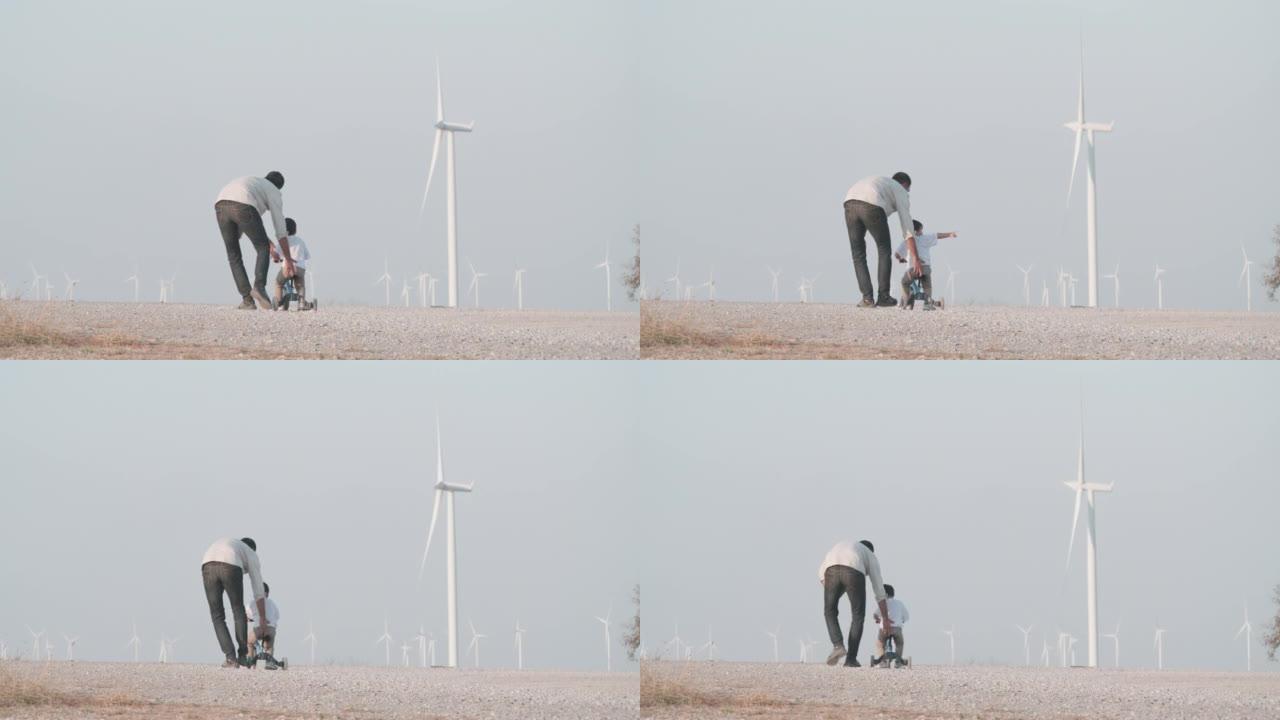 幸福的家庭父亲教2岁的孩子儿子在风力涡轮机之间自由地骑自行车。教孩子有关可持续发展的概念。