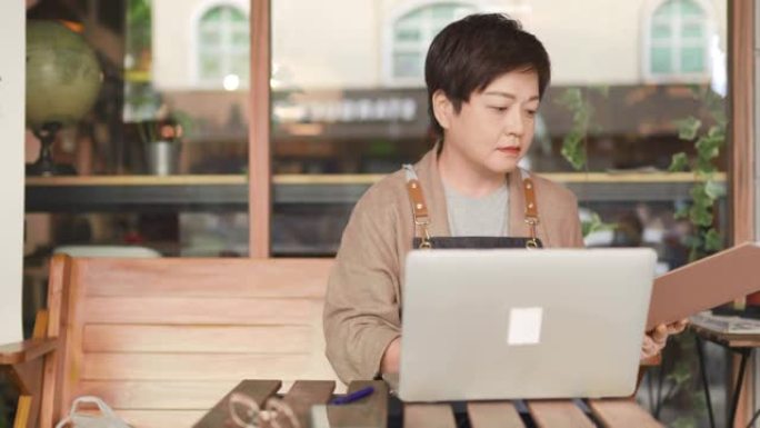 亚洲中国自助餐厅的女老板在咖啡馆餐厅外使用笔记本电脑检查财务账单