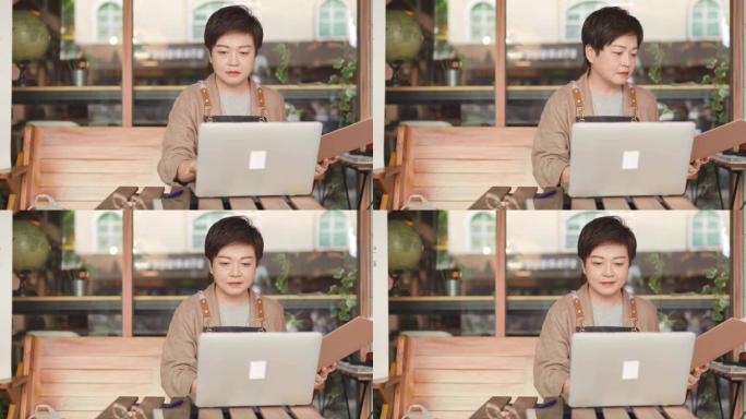亚洲中国自助餐厅的女老板在咖啡馆餐厅外使用笔记本电脑检查财务账单