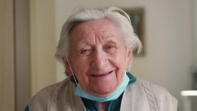 退休的残疾白发老年妇女的真实电影特写镜头正在脱下防护医用口罩，在家对着镜头微笑。新型冠状病毒肺炎、医