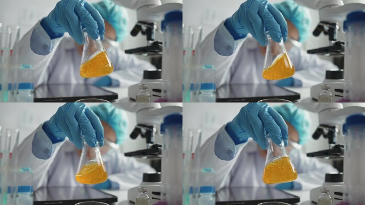 科学家戴着手套的手拿着黄色液体的无菌烧瓶。石油研究与有毒液体概念