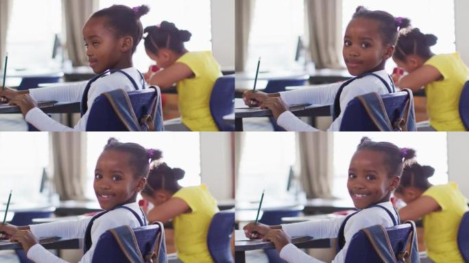 快乐的非洲裔美国女学生坐在教室里做笔记，看着相机的肖像