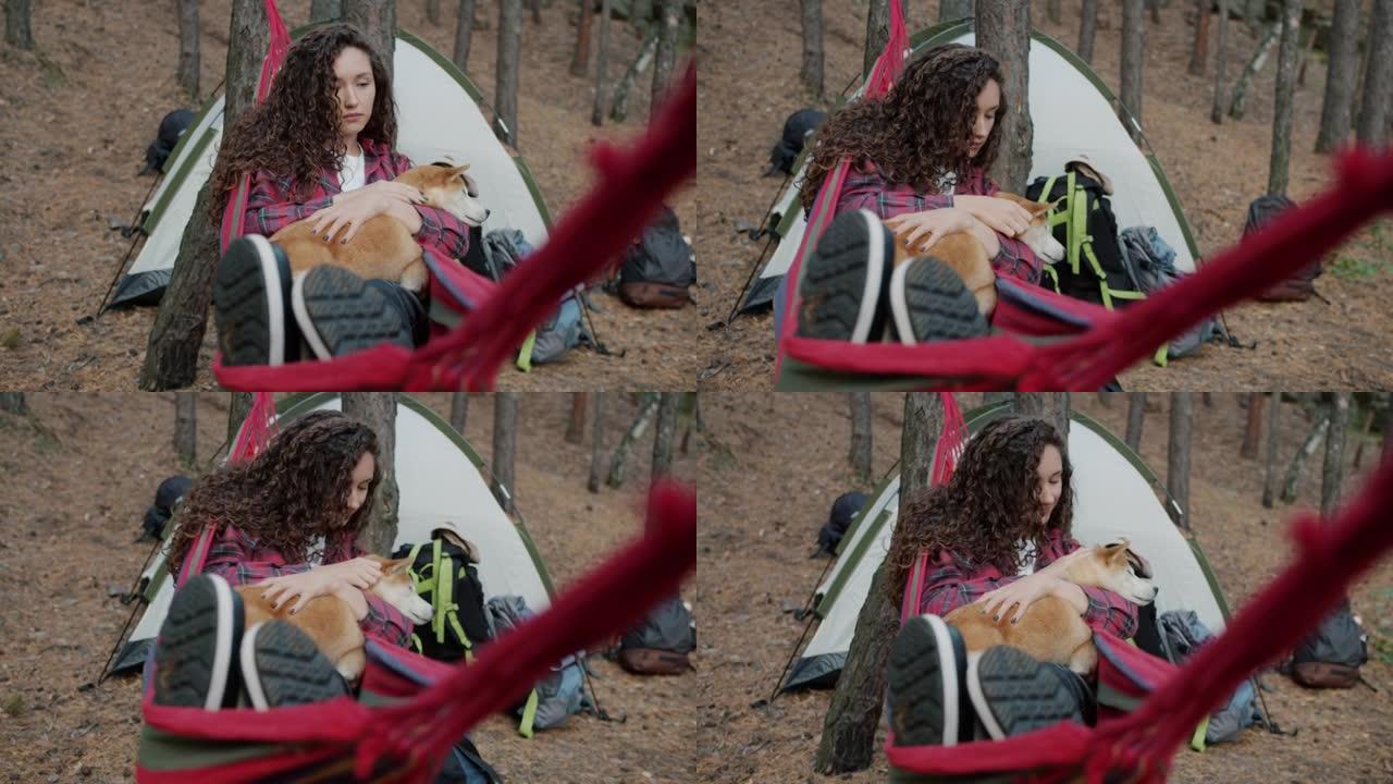 快乐的女游客在吊床上放松爱抚可爱的柴犬在秋天的森林里享受和平