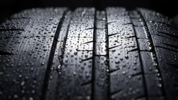 一个湿汽车轮胎滚动胎面花纹的特写工作室镜头，一个全新的街道轮胎上有水滴