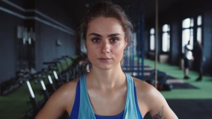 放大年轻有吸引力的坚定女运动员看着相机，在健身俱乐部锻炼后满头大汗。