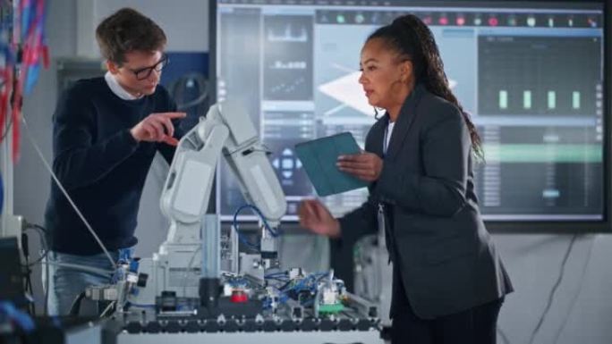 黑人女总工程师拿着平板电脑，与男学生交谈，而机器人手臂在上课时在他们的监督下移动。计算机科学教育与学