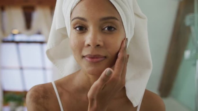 混合种族妇女的肖像头上戴着毛巾在脸上涂上奶油