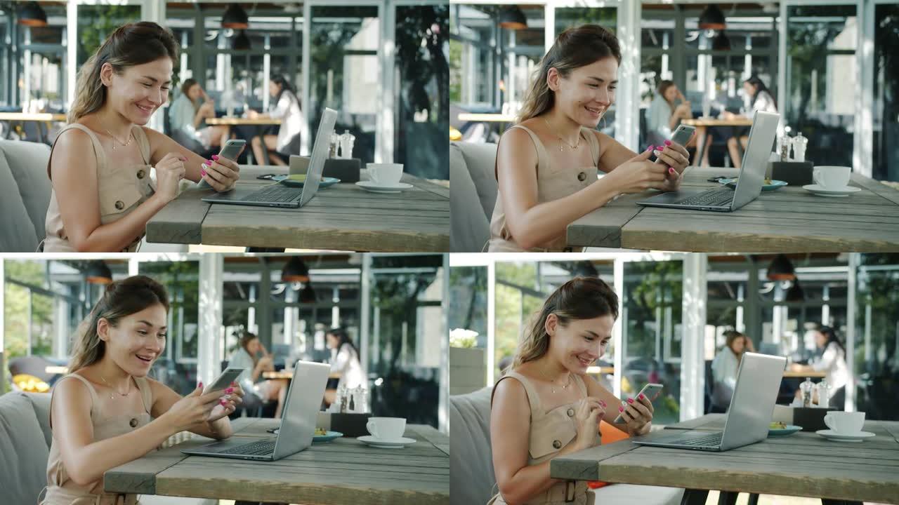 快乐的女孩自由职业者的肖像，用笔记本电脑工作，然后看着智能手机屏幕笑着