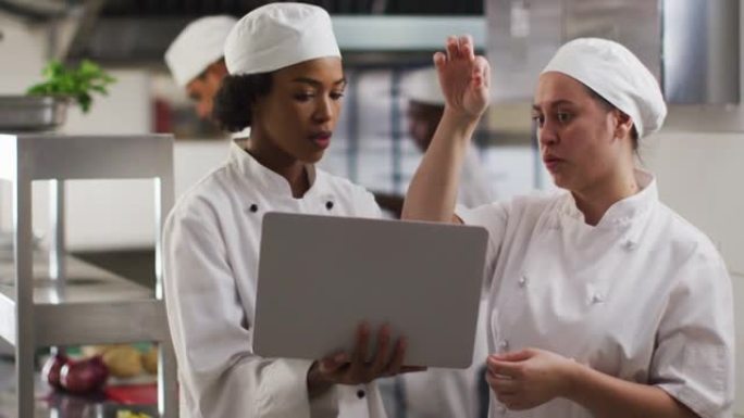 两位不同的女厨师在餐厅厨房里交谈和使用笔记本电脑
