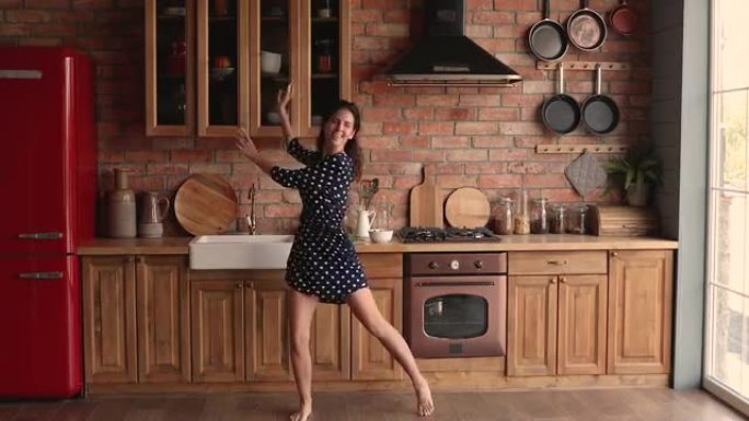 穿着漂亮的幸福女人独自在舒适的厨房跳舞