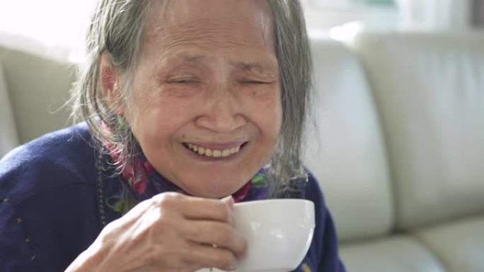 亚洲高级妇女正在喝热茶并看着相机