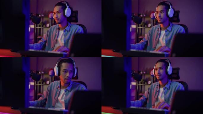 快乐亚洲男玩家戴着耳机参与玩视频游戏彩色霓虹灯电脑，晚上在客厅的平板电脑上录制播客现代房子。