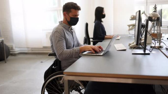 大流行期间坐在轮椅上的男子在办公桌前工作