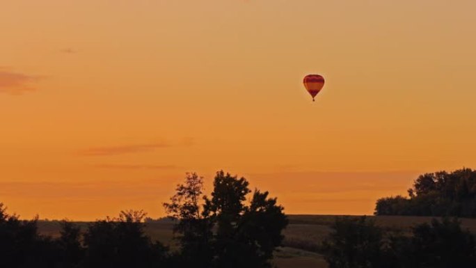 在橙色日落天空中，热气球在乡村田野上空飞行