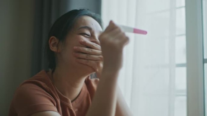 快乐的亚洲女人在检查妊娠试验后感到快乐，结果为阳性