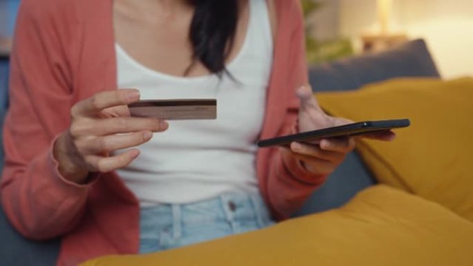 夜晚美丽微笑的亚洲女士在客厅沙发上使用手机订购带信用卡的网上购物产品。