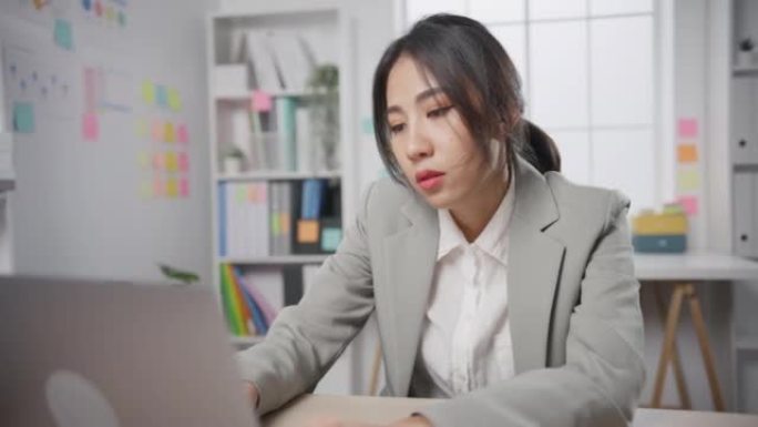 年轻的亚洲女商人坐在办公室里，笔记本电脑过度劳累，倦怠综合症。