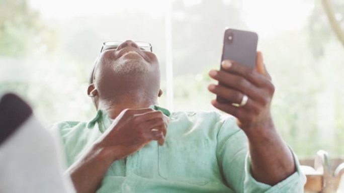快乐的非洲裔美国老人坐在脚上，用智能手机进行视频通话，大笑