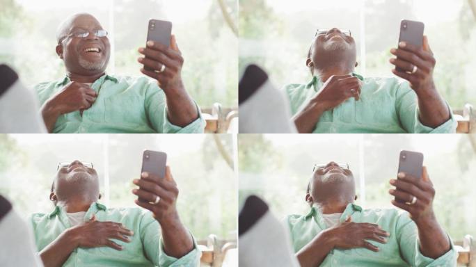快乐的非洲裔美国老人坐在脚上，用智能手机进行视频通话，大笑