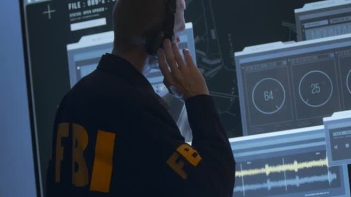 戴着耳机的联邦调查局特工在他前面的一个大HUD屏幕上工作，我们从背部和腰部以上看到他