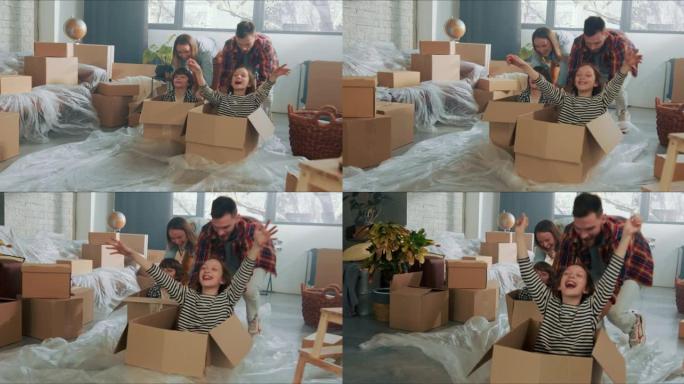 年轻有趣快乐的父母推动兴奋可爱的孩子在地板上的纸箱庆祝搬进新公寓。